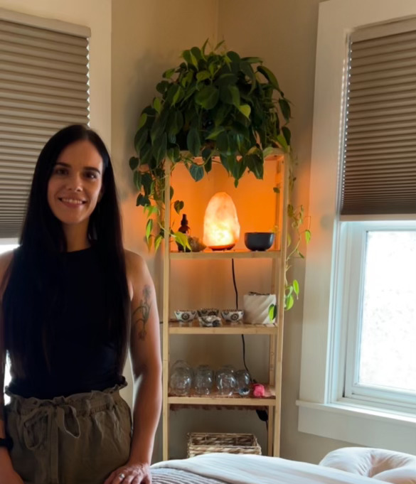 Woman standing next to massage bed with shelves behind her.